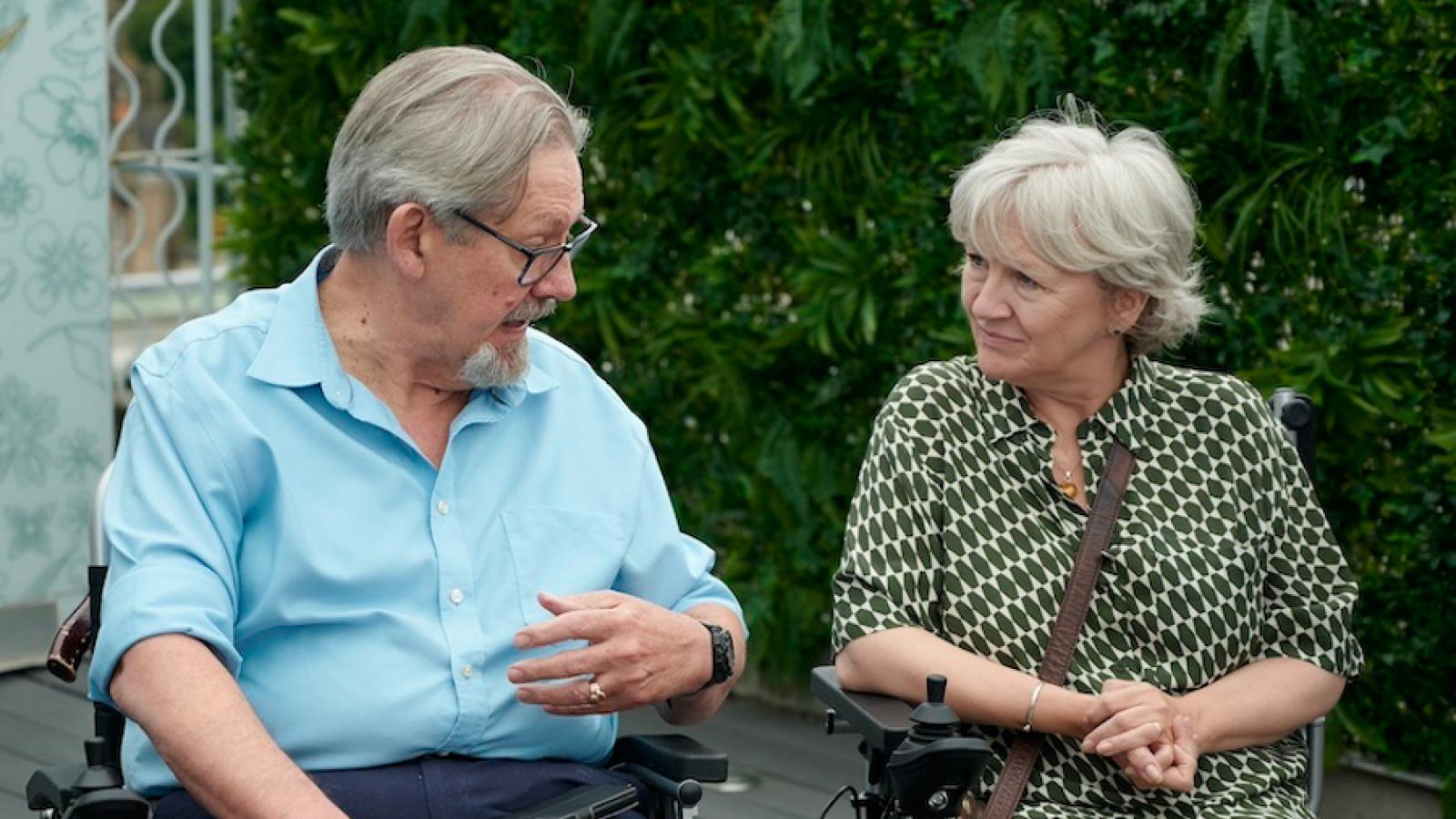 Two people sit in wheelchairs next to one another