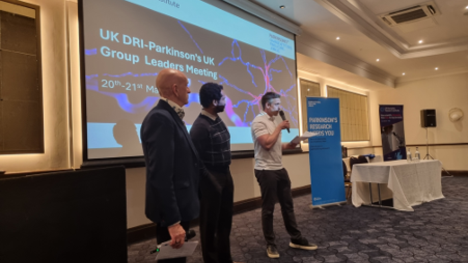 Three people stand at the front of a room at a conference