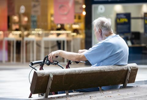 A man with a walking aid sits on a public bench