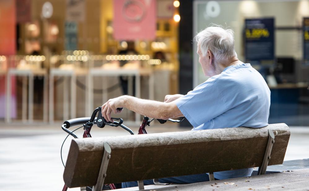 A man with a walking aid sits on a public bench